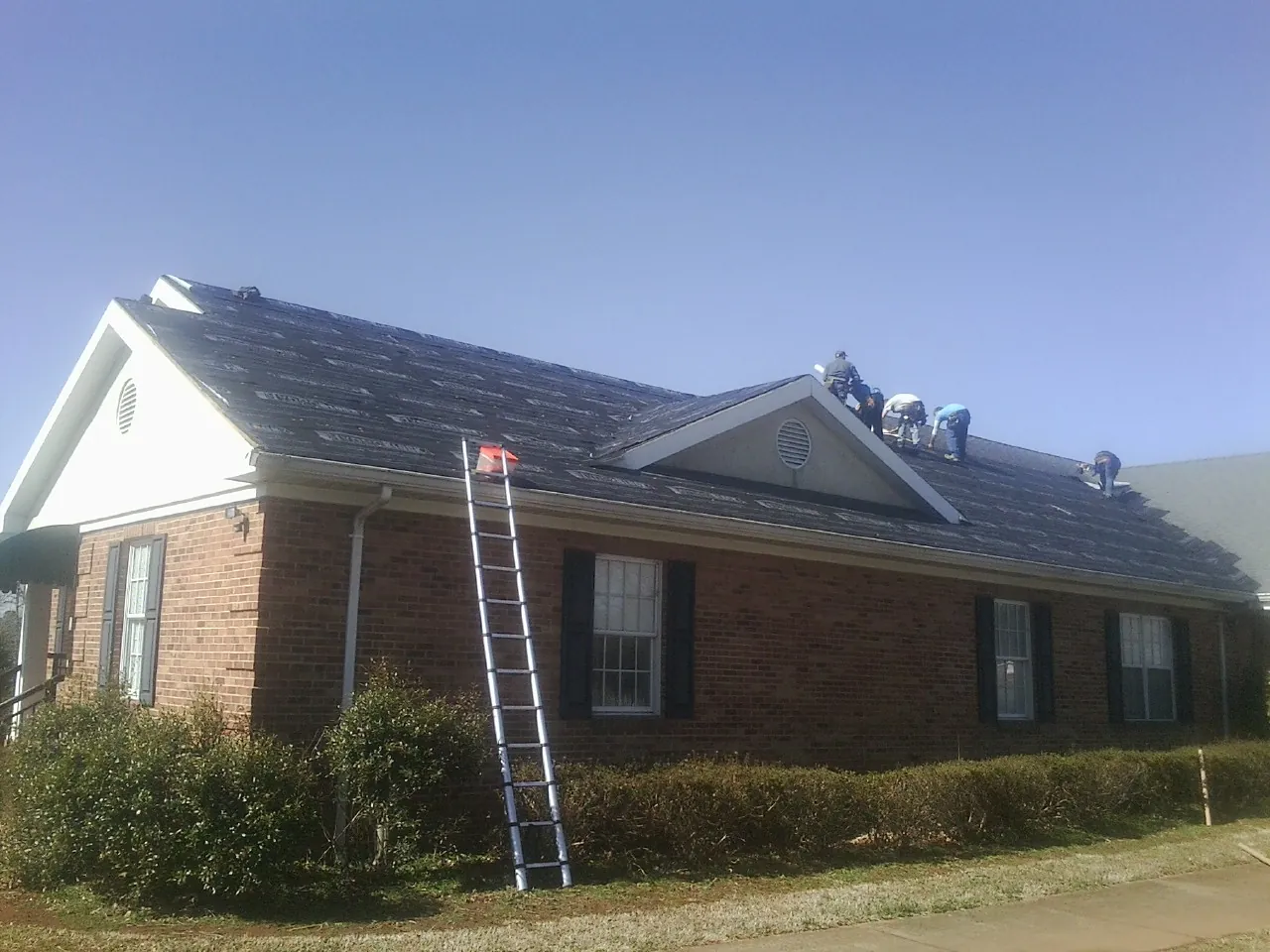 Crew tearing shingles off a brick ranch roof with a ladder set — Emergency Roof Repair work by our crew in Stonington