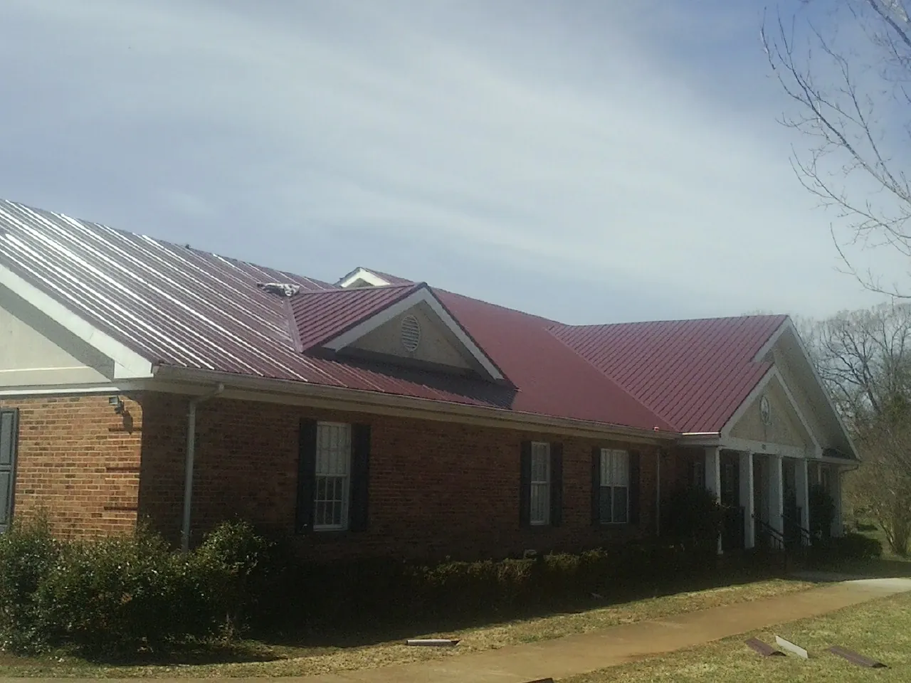 Red metal roof with gabled entries on a long brick building, from a Hail Damage Roof Repair job in Stonington