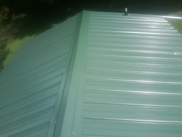 New green metal panels meeting at the ridge of a roof — Flat Roof Repair work by our crew in Stonington