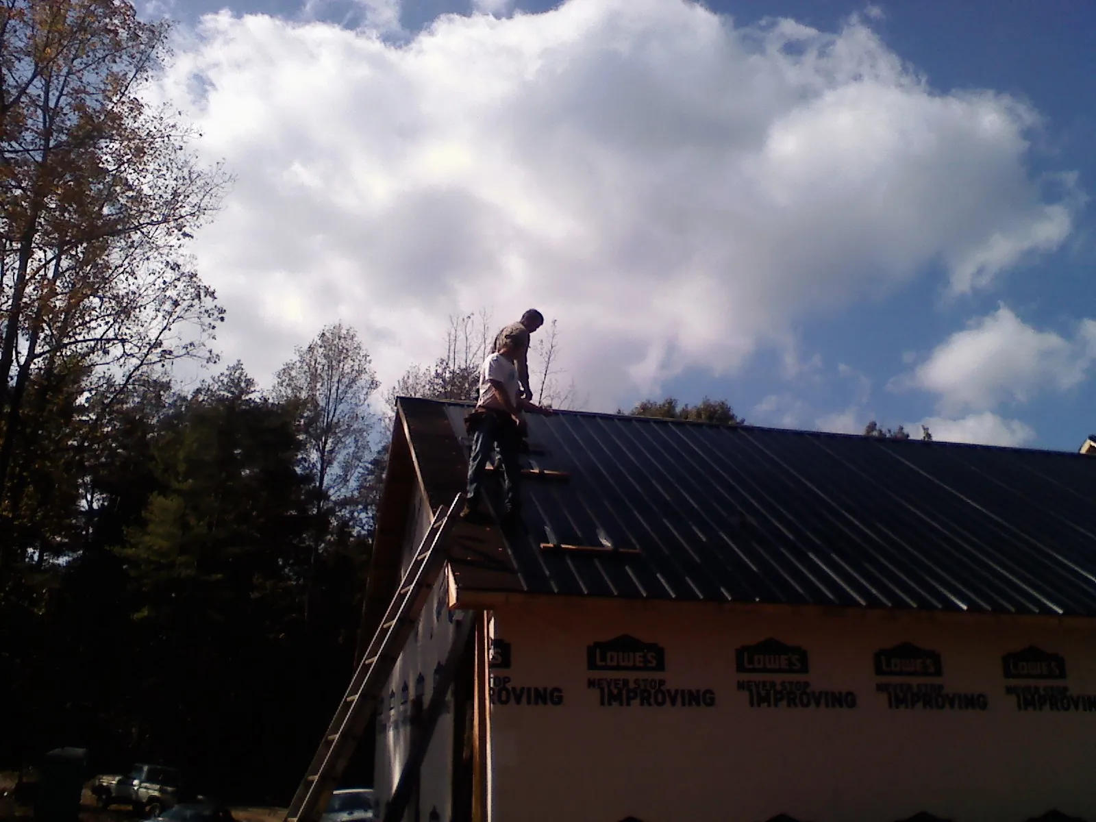 Roofer fastening dark metal panels high against a cloudy sky, from a Roof Inspection job in Stonington